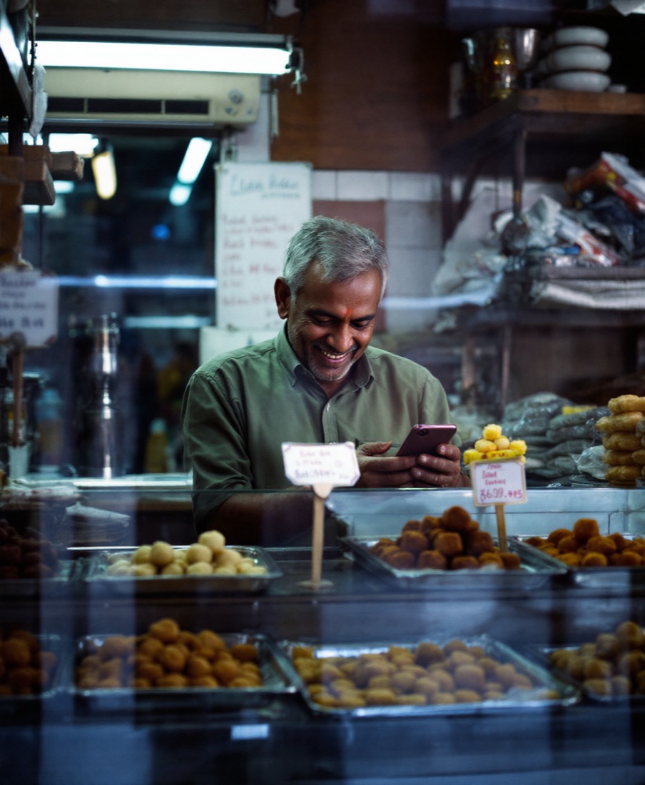 A sweet shop owner behind his counter, smiling at his phone